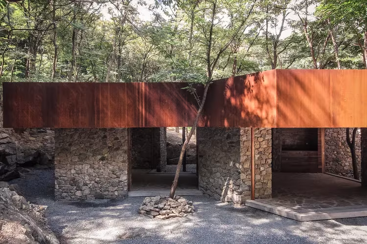 Estudio TAO (Trace Architecture Office). Rockview Teahouse, situada en el Parque Tashan, Fachada de acero corten de la Rockview Teahouse sobre pilares de piedra y patio de grava con árboles