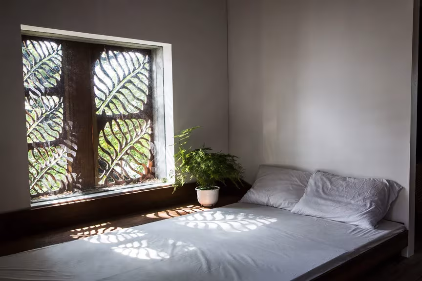 Thong house, paneles están tallados con motivos de hojas. Dormitorio Dormitorio de la Thong House con cama baja y ventana de celosía en forma de hojas que proyecta sombras