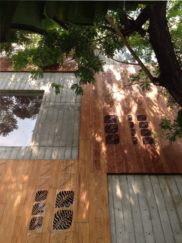 Paneles de madera calados con motivos de hojas en la fachada de la Thong House bajo un árbol
