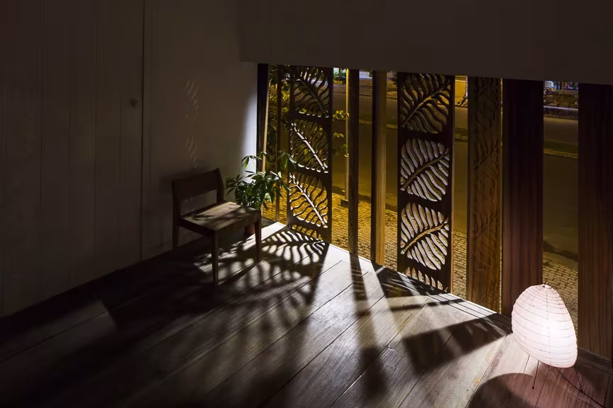 Thong house, paneles están tallados con motivos de hojas Estancia en penumbra de la Thong House con silla de madera, lámpara de papel y celosías con luz