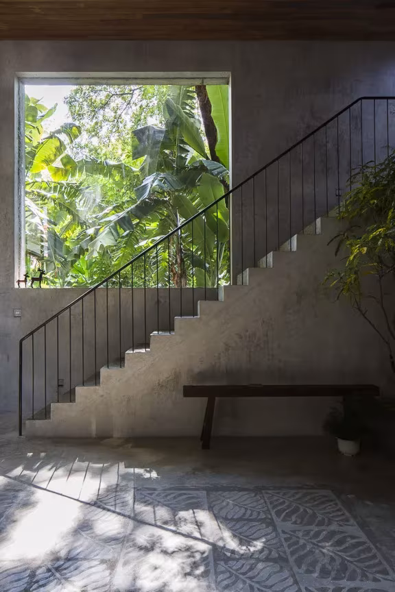 Shunri Nishizawa optó por vertebrar la vivienda en torno a una escalera central Escalera de hormigón con barandilla fina en la Thong House junto a una ventana cuadrada con vegetación