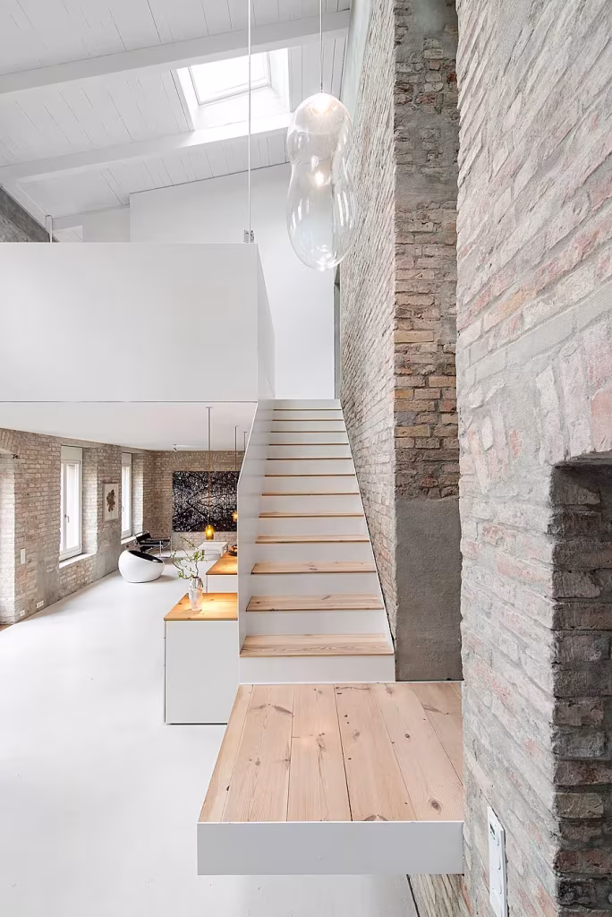 Escalera blanca con peldaños de madera de pino junto al muro de ladrillo en la Casa MMB de asdfg Architekten