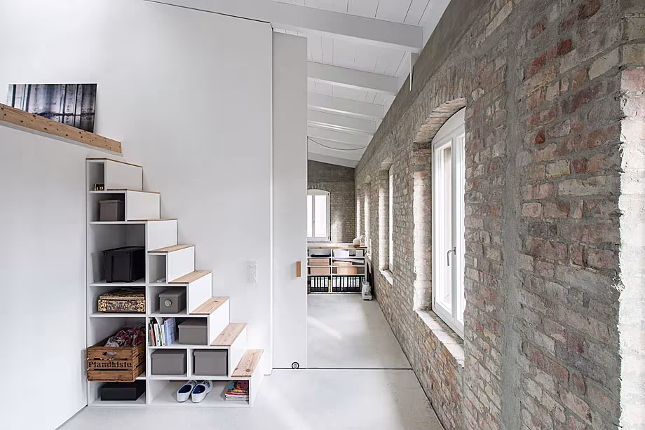 Escalera con almacenaje bajo los peldaños y ventanas alineadas junto al muro de ladrillo de la Casa MMB