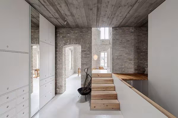 Altillo con escalera de madera, armarios blancos y techo de hormigón entre los muros de ladrillo de la Casa MMB