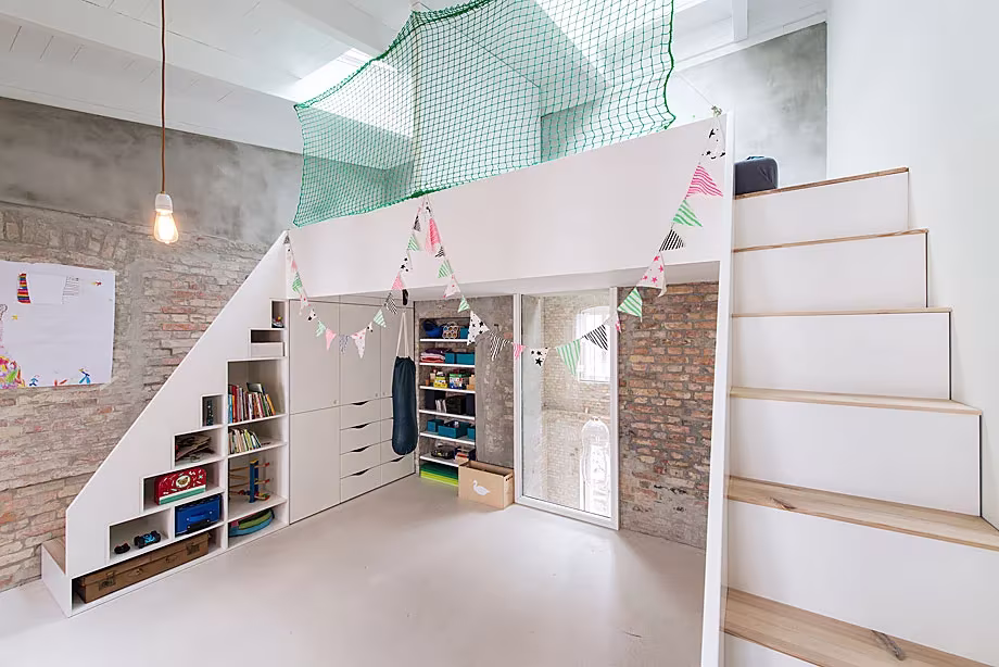 Cuarto infantil con altillo blanco, red verde y guirnaldas sobre armarios bajo la escalera, en la Casa MMB