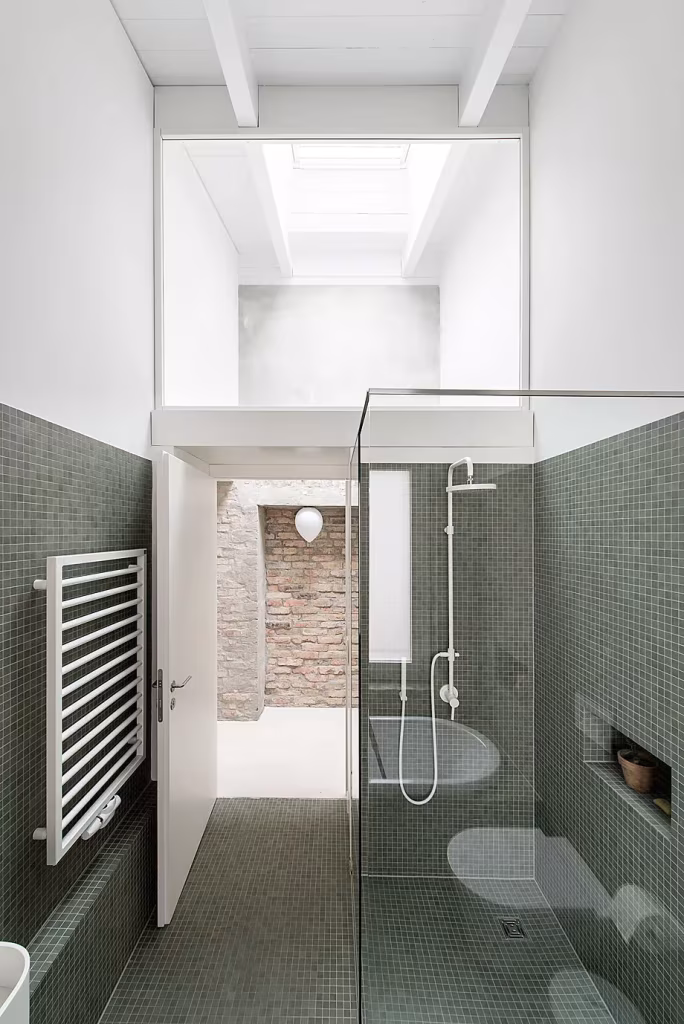 Baño estrecho con mosaico verde, ducha acristalada y lucernario bajo una altura doble en la Casa MMB de Berlín