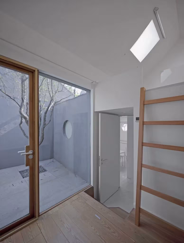 Split Courtyard House. TAO. acristalamiento y claraboya Estancia blanca de la Split Courtyard House con escalera de madera y puerta acristalada al patio