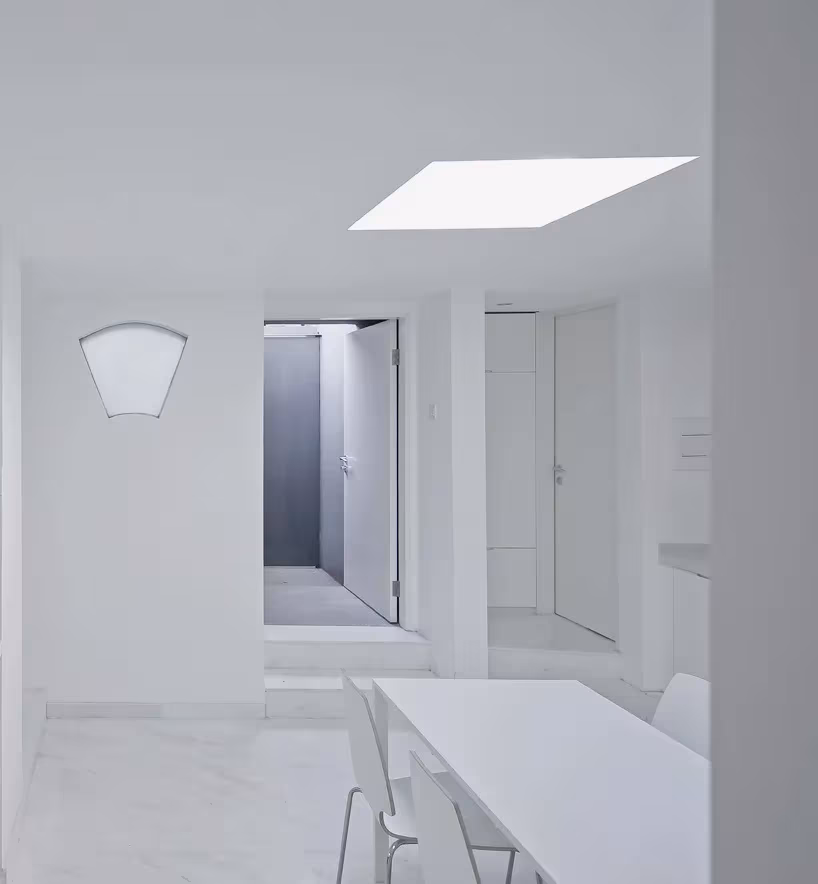 Split Courtyard House. TAO. superficies blancas contemporaneo Interior blanco de la Split Courtyard House con lucernario, mesa y ventana en forma de abanico