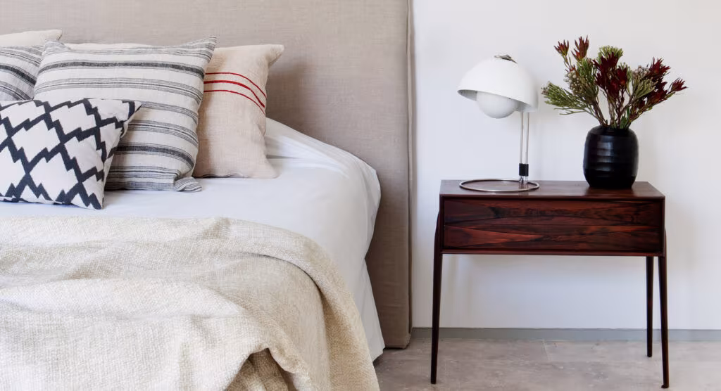 Dormitorio de estilo escandinavo con mesilla de madera oscura, lámpara blanca y cojines de rayas