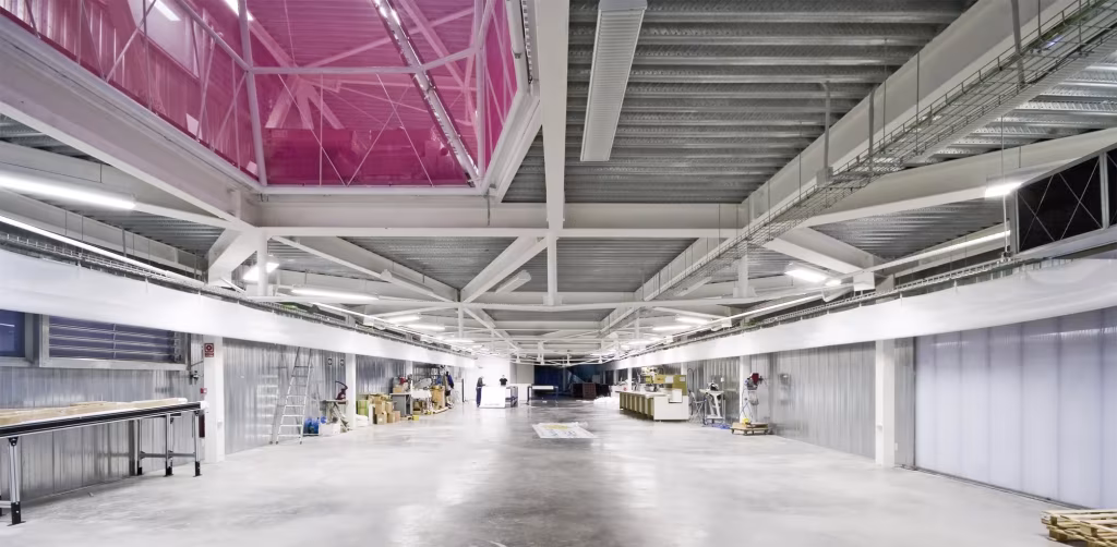 Nave industrial Diagonal 80 con estructura metálica blanca, lucernarios magenta y suelo de hormigón