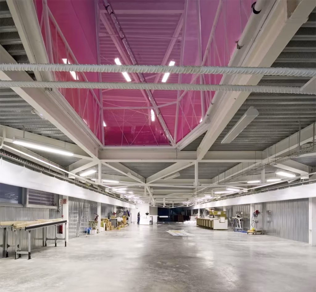 proyecto de Amid.Cero9 en Guadalix. acabados industriales interiores Interior diáfano de Diagonal 80 con cerchas metálicas bajo una cubierta de luz rosada y puestos de trabajo