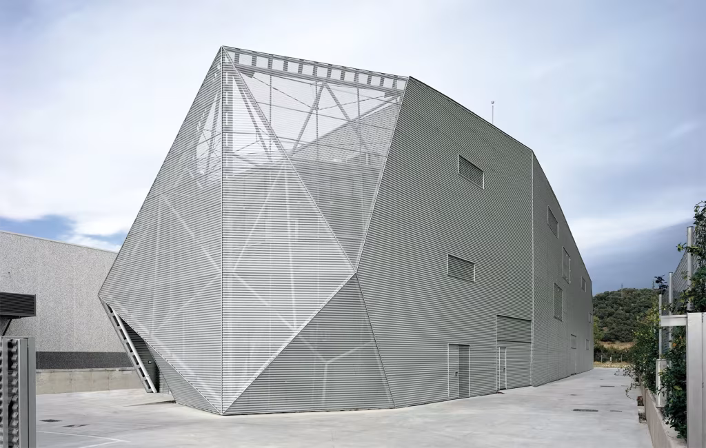 Diagonal80. Proyecto de Amid.Cero9. exterior limitado por el entorno Fachada poliédrica de Diagonal 80 revestida de chapa y malla plateada junto a un patio de acceso