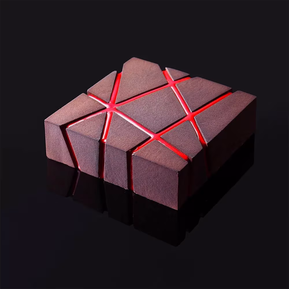Postre geométrico de Dinara Kasko de forma cúbica granate con grietas rojas brillantes sobre fondo negro