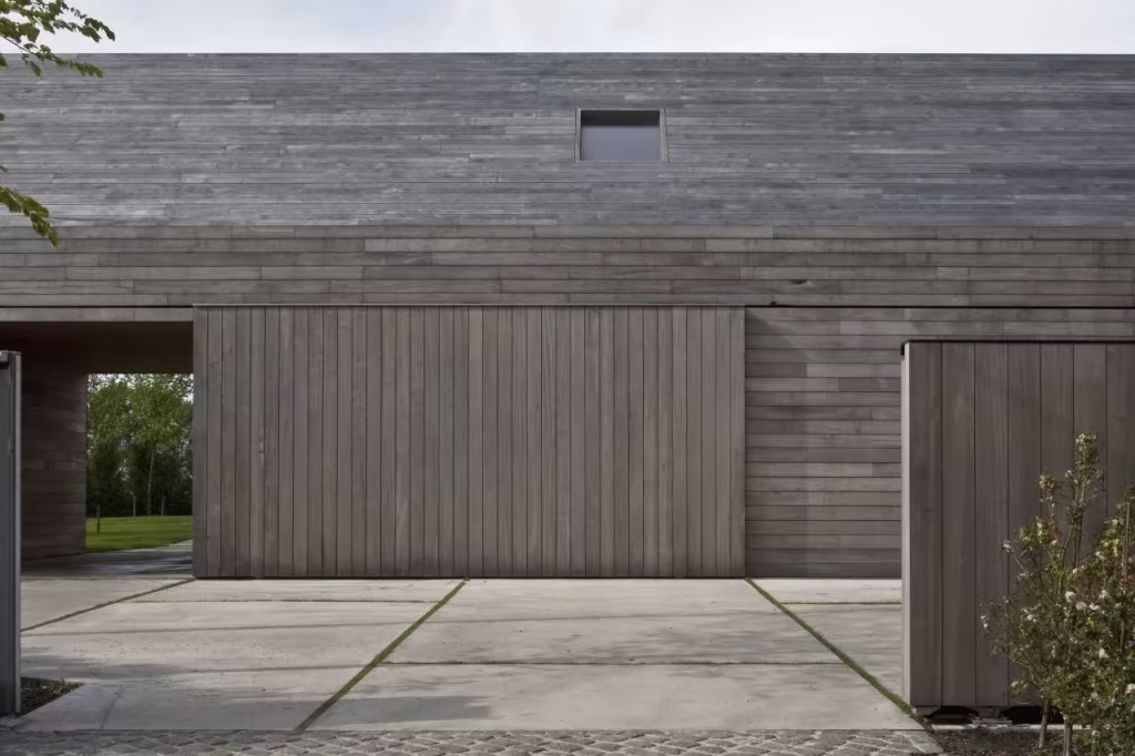 Fachada de tablas de madera gris con puertas correderas y pequeños lucernarios en la Casa DC II