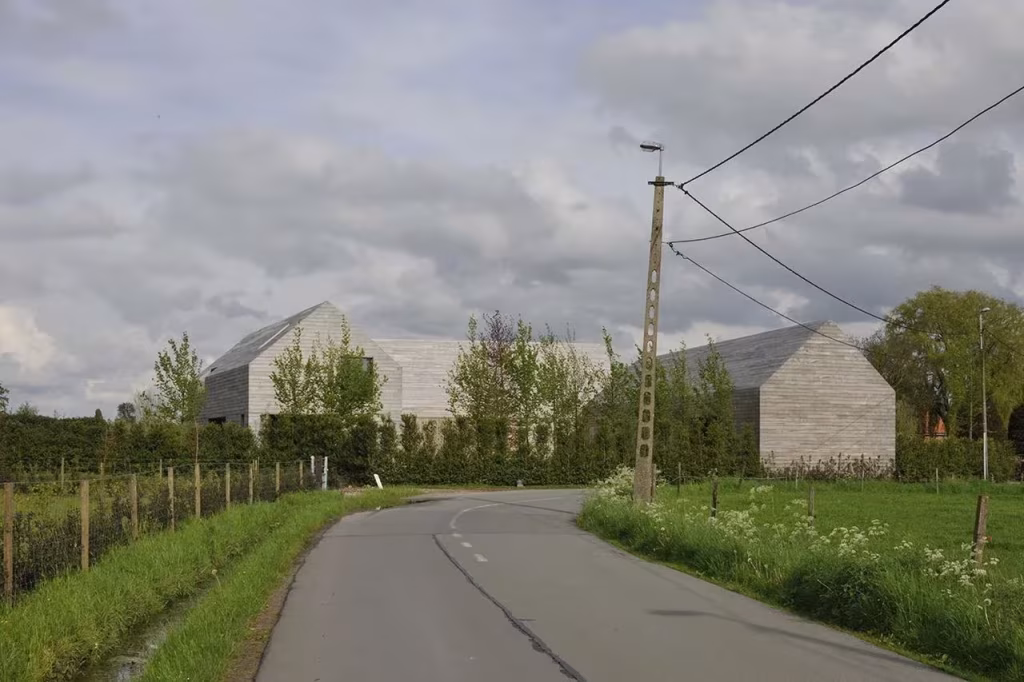 Casa DC II entre campos vista desde la carretera rural, con su silueta de granero de madera gris