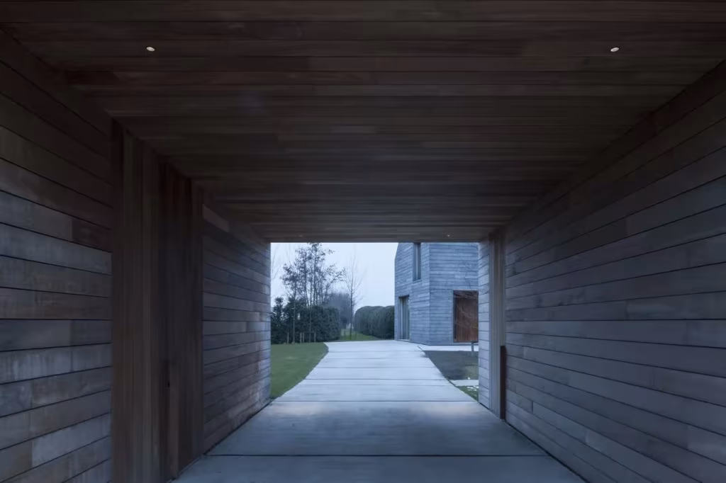 Paso cubierto de madera oscura que enmarca el jardín y el camino de hormigón en la Casa DC II