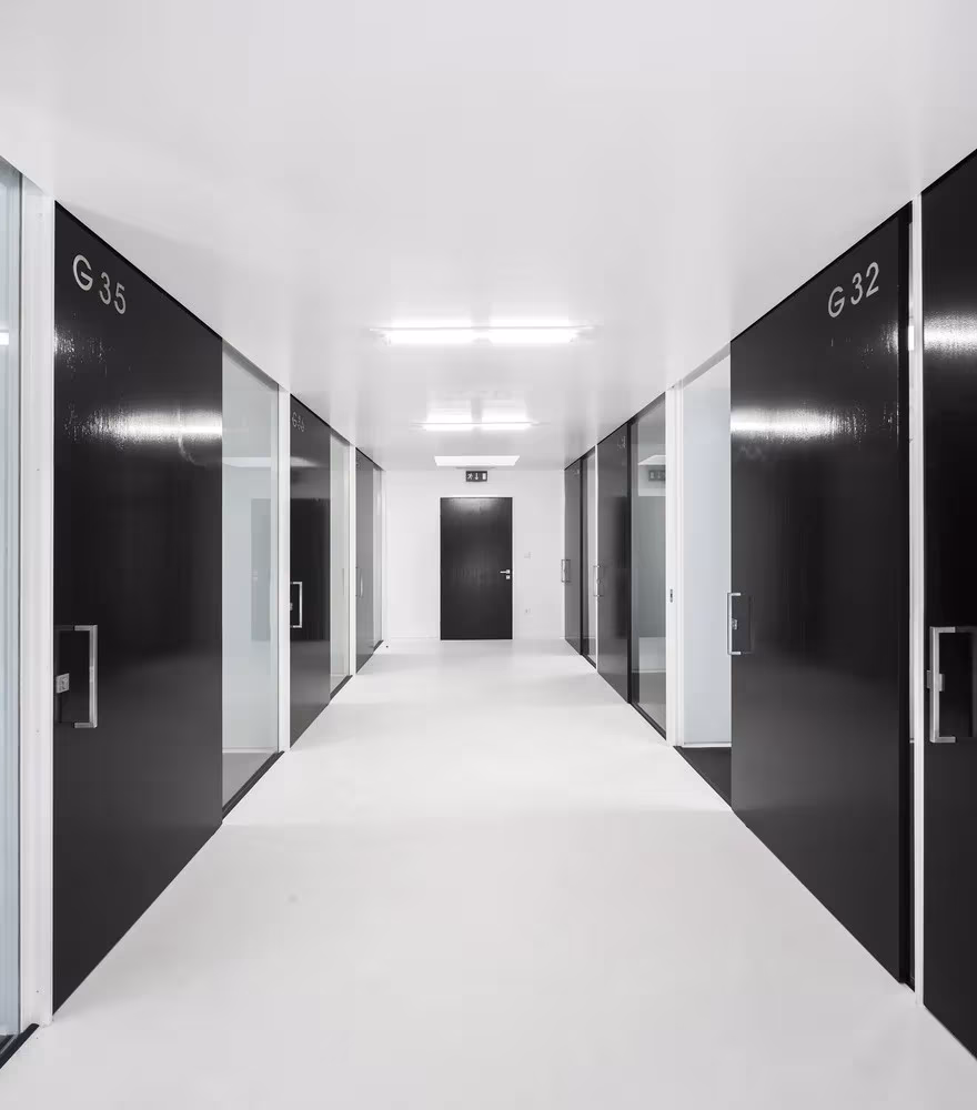 Corredor blanco de la ESTIG de Beja flanqueado por puertas negras y paños de vidrio