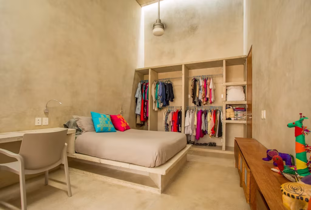 Dormitorio de paredes de mortero con armario abierto, cama baja y ropa de colores en la Casa Gabriela