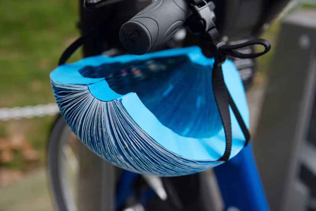Casco plegable EcoHelmet de papel azul en forma de acordeón colgado del manillar de una bicicleta