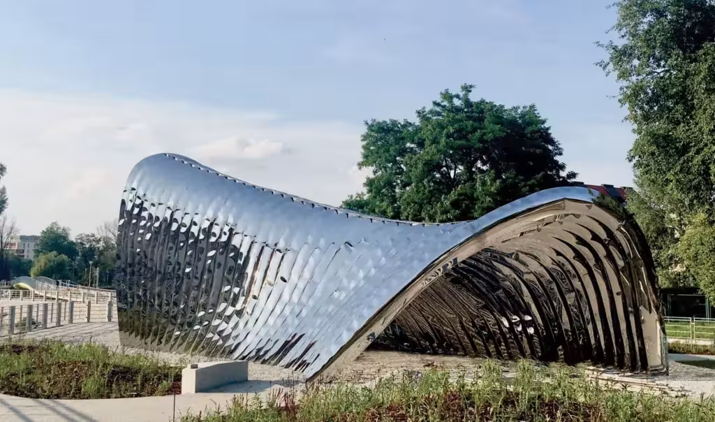 Escultura NAWA de Oskar Zieta, un arco ondulado de acero inoxidable brillante sobre una isla con árboles en Wroclaw
