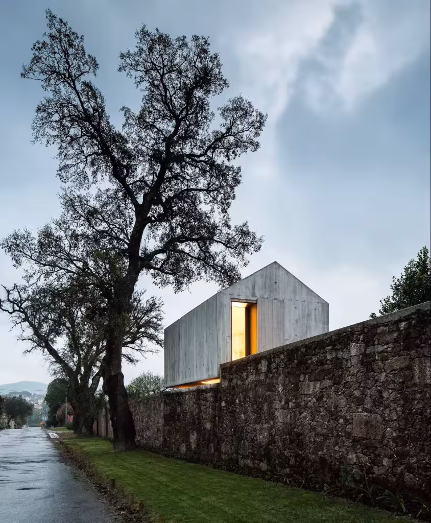 The Dovecote por AZO Sequeira Arquitectos Associados. The Dovecote de AZO Sequeira Arquitectos tras el muro de piedra, entre árboles y con la ventana encendida
