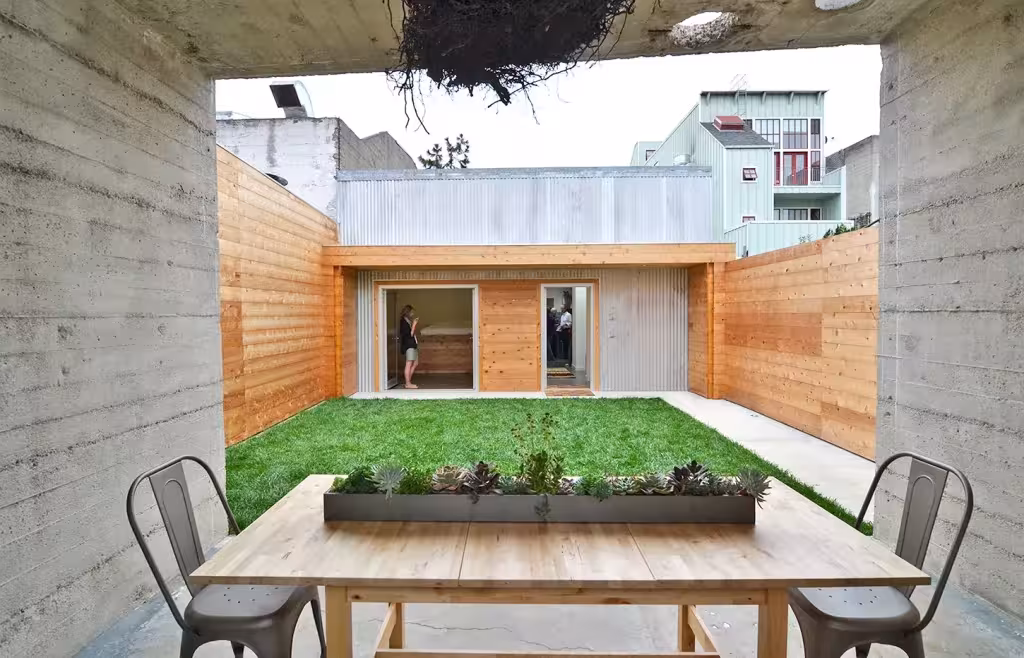 Shotwell Residence de Todd Davis Microondulado, metal corrugado Mesa de comedor ante el patio de césped y el muro de madera visto desde el pabellón de hormigón de la Shotwell Residence