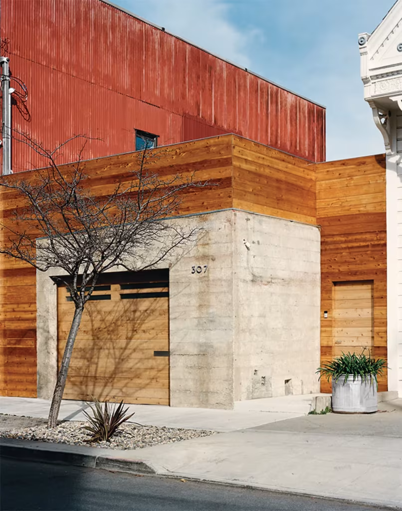 Shotwell Residence de Todd Davis con edificio vecino Esquina de la Shotwell Residence con volumen de hormigón, revestimiento de madera y chapa roja sobre el garaje