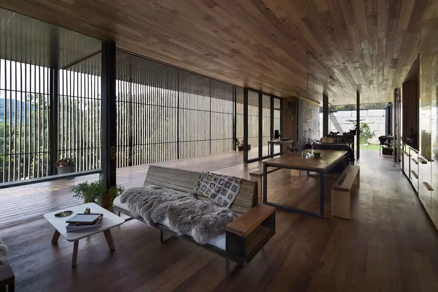 Salón comedor de la Sawmill House con sofá, mesa y celosía de lamas verticales ante el valle