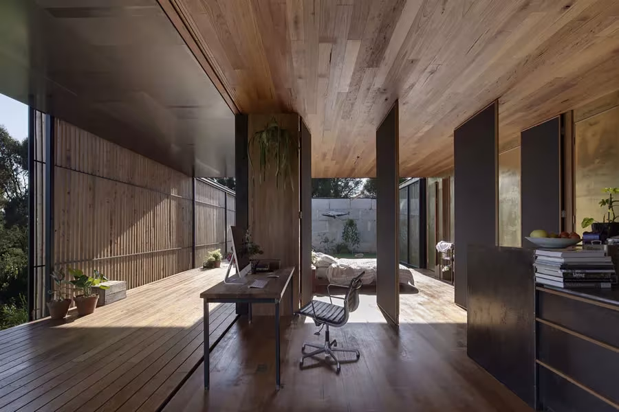 Zona de trabajo de la Sawmill House con escritorio, pilar de madera y suelo de tablas bajo techo de madera