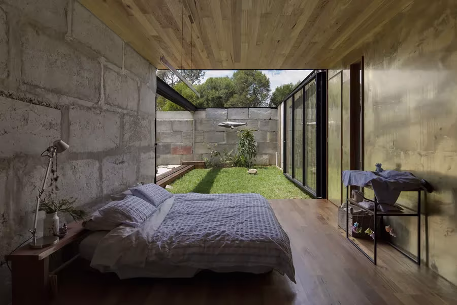 Dormitorio de la Sawmill House con muro de bloques de hormigón y patio de césped visible tras la cama