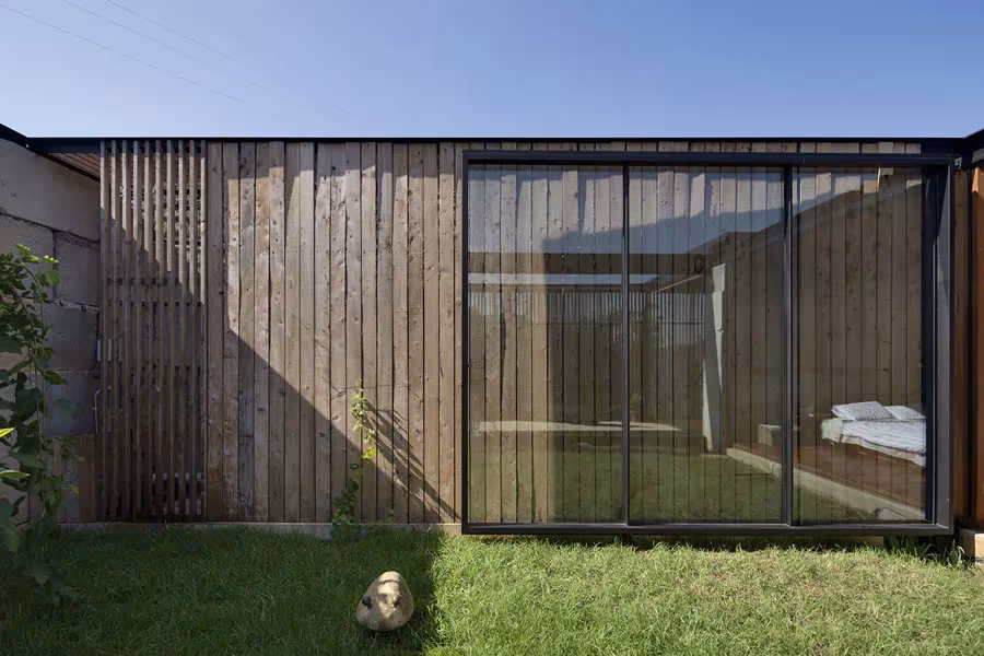 Fachada de tablones de madera y puertas correderas de vidrio de la Sawmill House sobre el césped