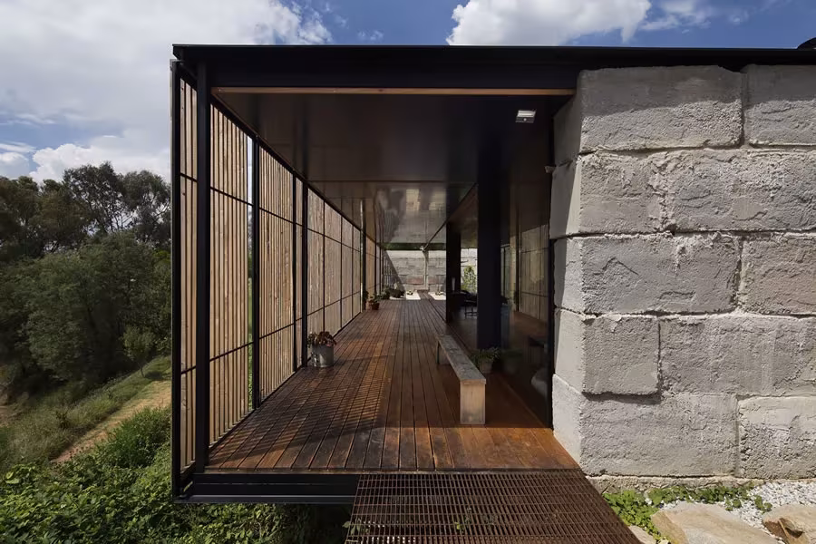 Pasarela de entrada de la Sawmill House con celosía de madera junto al muro de bloques de hormigón reciclado