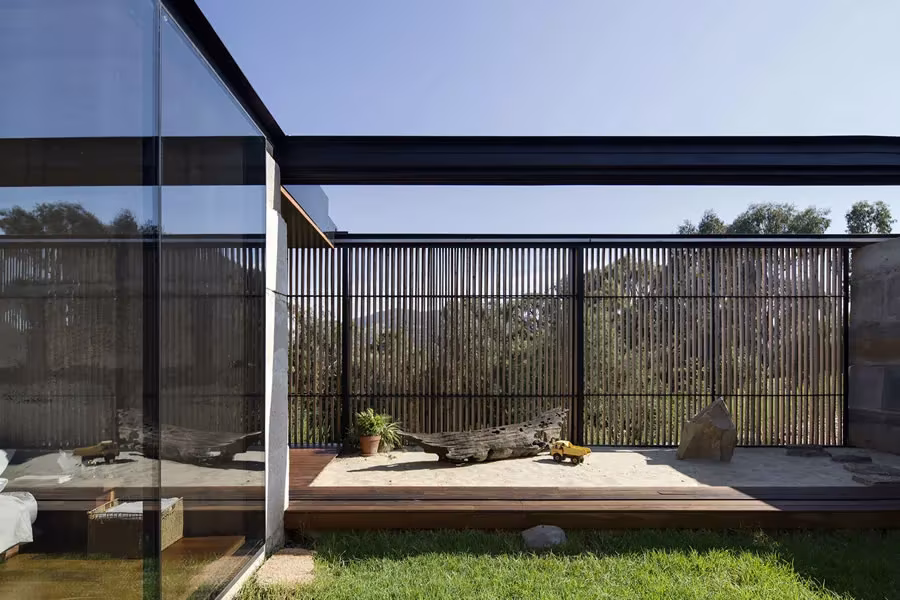 Terraza de la Sawmill House con celosía de lamas oscuras y cerramiento de vidrio abierto al paisaje