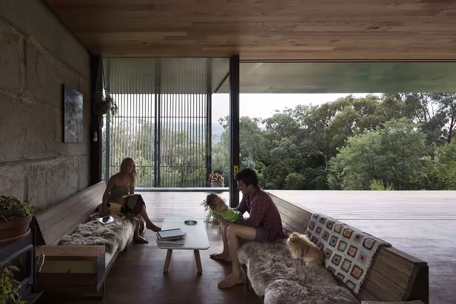 Salón de la Sawmill House con banco corrido, techo de madera y gran apertura al paisaje de eucaliptos