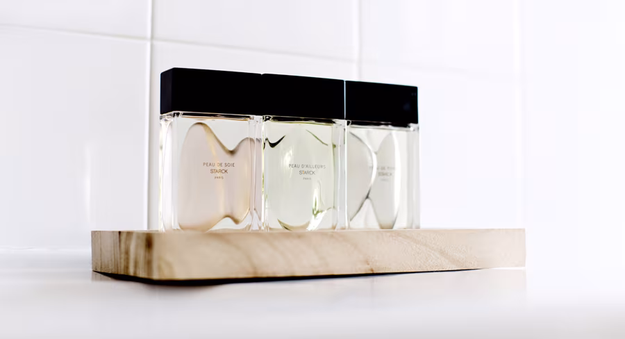 Tres frascos de perfume de Starck Paris con tapón negro sobre una base de madera