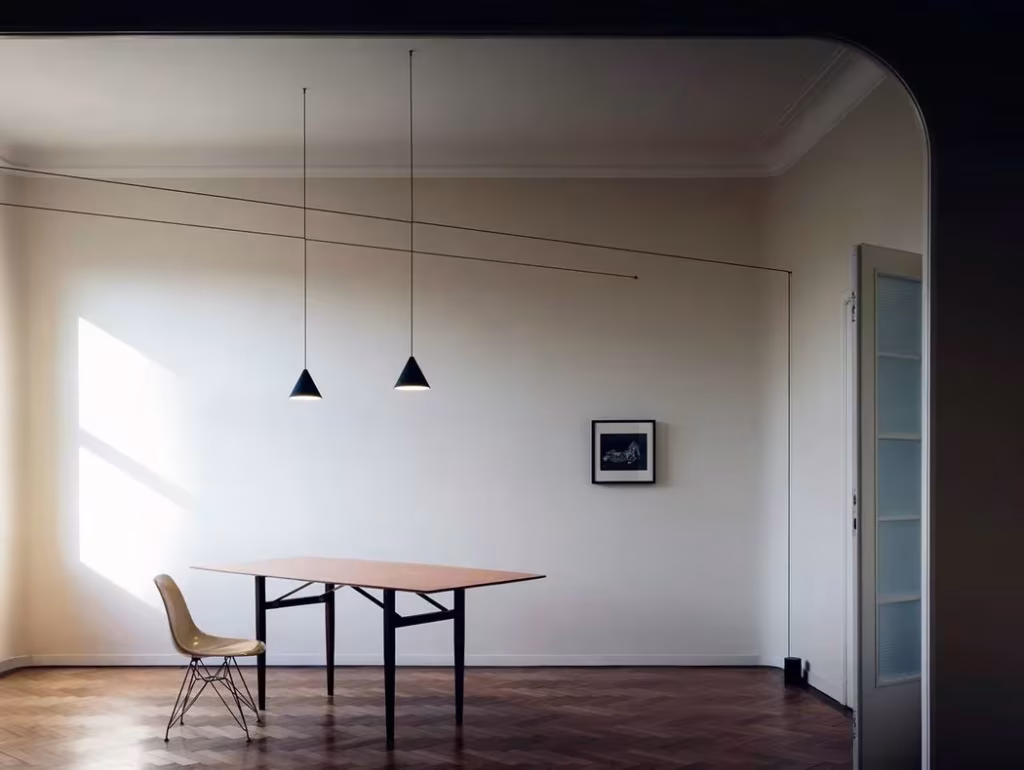 Lámparas String Lights de Michael Anastassiades con cables tensos y conos negros sobre una mesa de madera