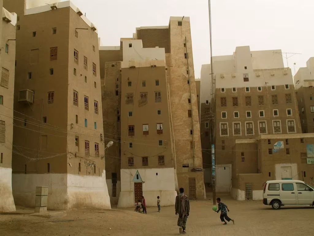 Niños jugando al pie de las torres de adobe de Shibam, con base encalada