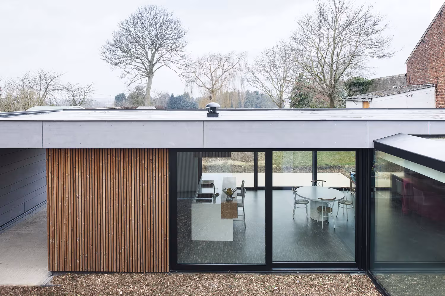 Fachada de lamas de madera y cristalera corredera con cocina y comedor en Goetsenhoven House, Tienen