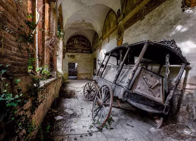 Carruaje fúnebre de madera deteriorado en una galería abovedada abandonada invadida por la hiedra