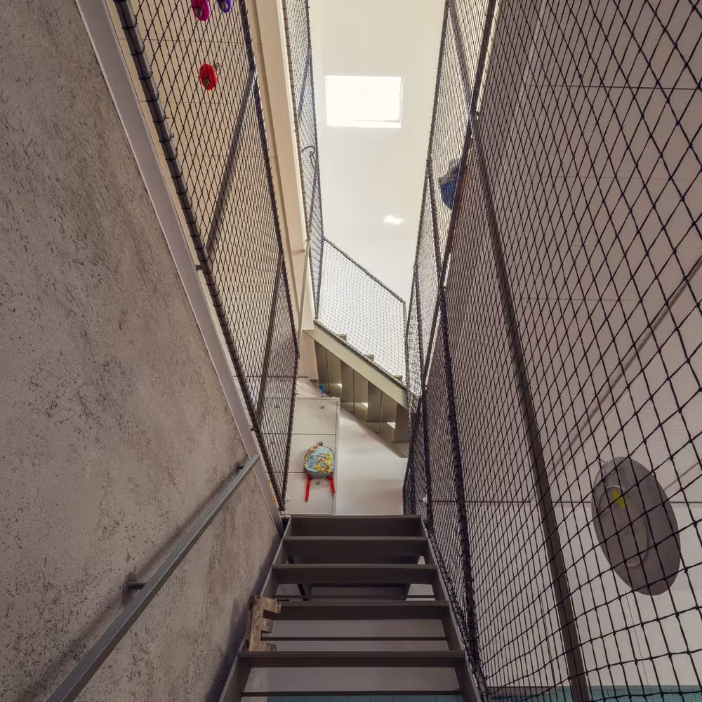 Escalera metálica entre un muro de mortero y una barandilla de malla en la Casa de Juno