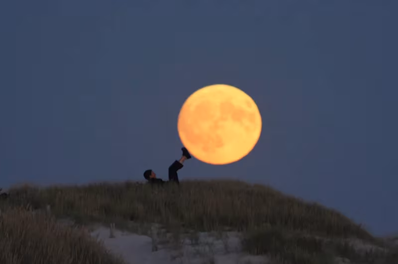 Luna llena naranja que parece alimentar a dos figuras sobre una duna en la serie Moon Games de Laurent Laveder