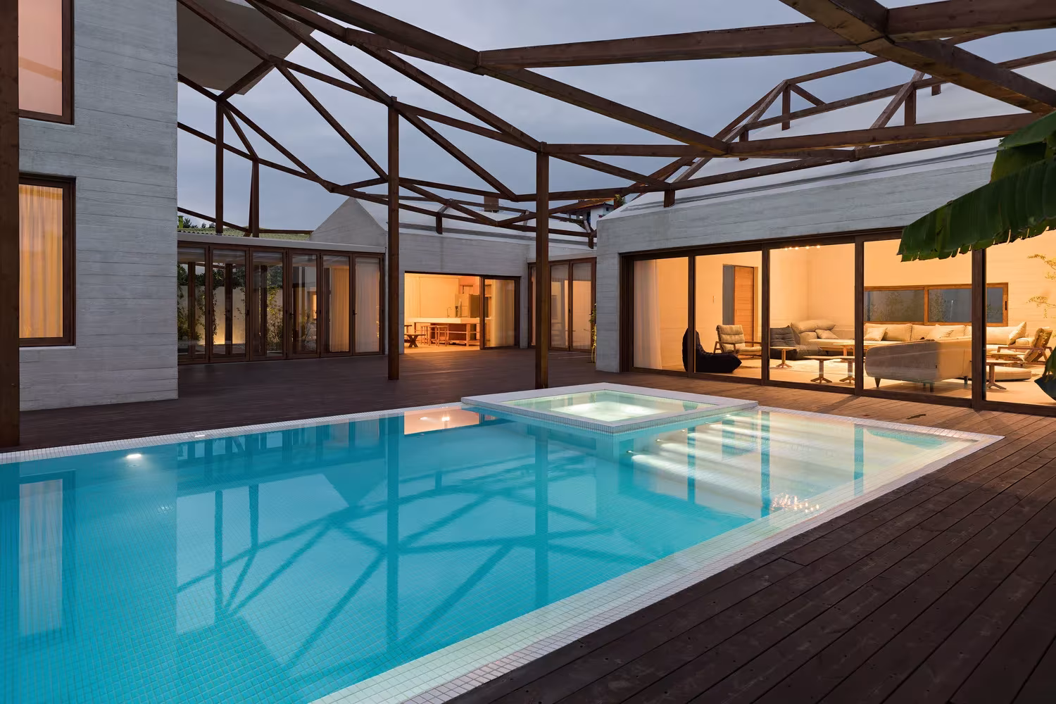 Piscina cubierta de Villa Vanoosh bajo una estructura de madera, con el salón iluminado al fondo, en Mazandaran