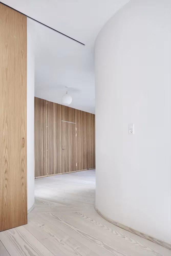Muro curvo blanco y panel de roble con puerta corredera en la Villa Platan de ADEPT
