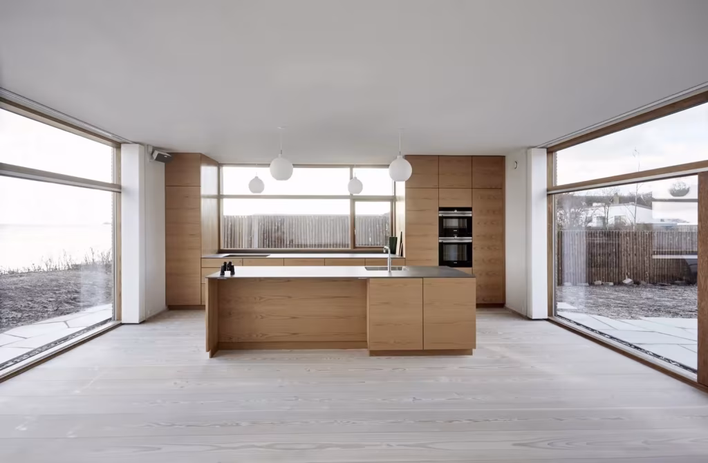 Cocina con isla de roble y ventanales de suelo a techo abiertos a la costa en la Villa Platan