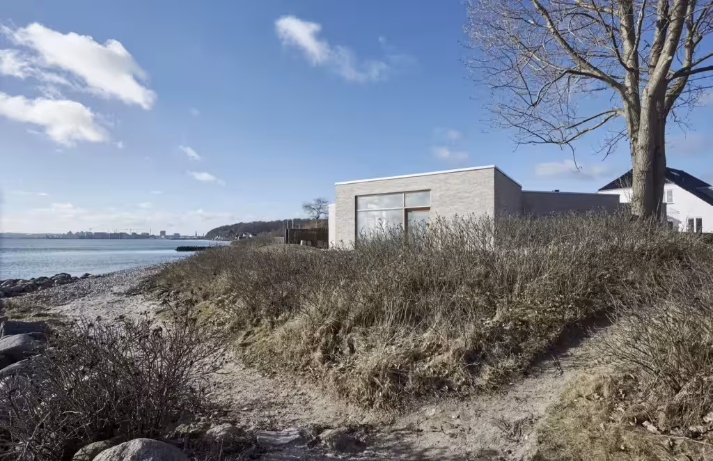Volumen de ladrillo de la Villa Platan tras las dunas de hierba y la orilla del mar danés