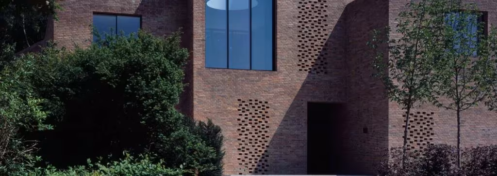 Fachada de ladrillo de la Highgate House con celosía calada y ventana alargada tras la vegetación del jardín