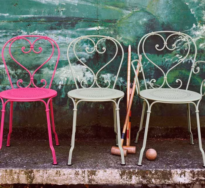 Sillas 1900 de acero lacado en rosa y verde claro con respaldo de volutas ante un muro pintado