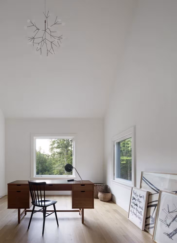 Despacho blanco con escritorio de madera, silla negra y ventanas al bosque en Undermountain