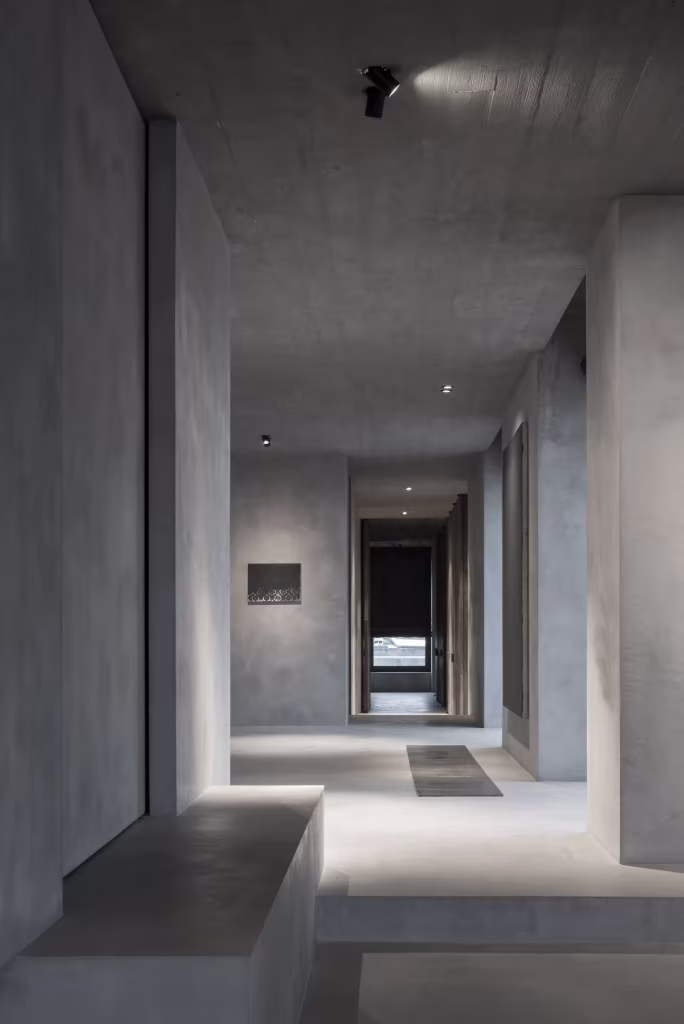 Vestíbulo del C Penthouse con volúmenes de cal gris, banco de obra y perspectiva hacia el interior de la vivienda