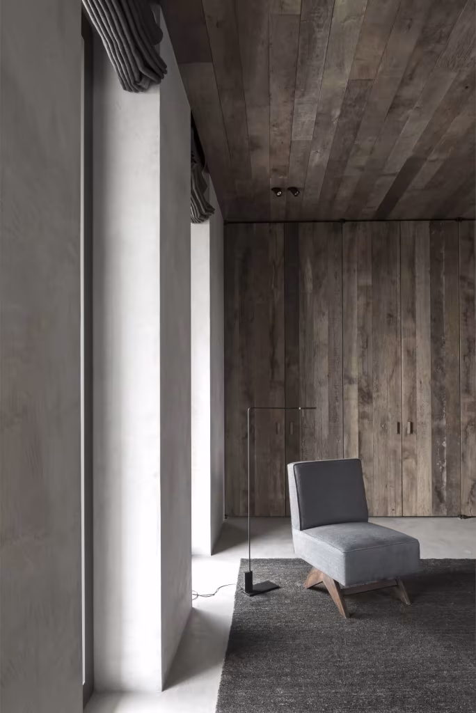 Rincón de lectura con butaca gris, ventanal y techo de madera recuperada en el C Penthouse de Van Duysen